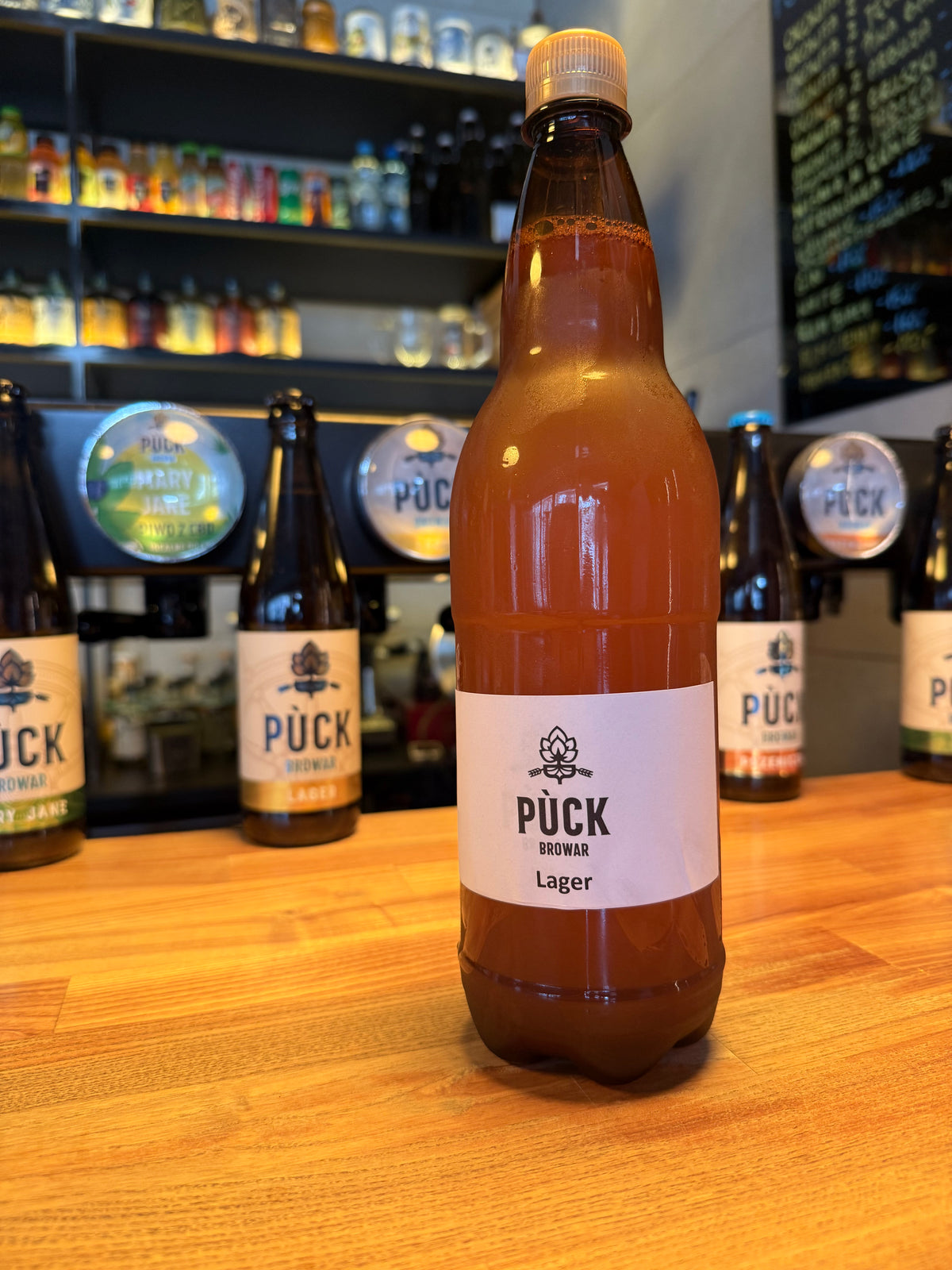 Butelka litrowego piwa rzemieślniczego Pùck Browar Lager zaprezentowana na drewnianym blacie barowym w Browarze Puck.