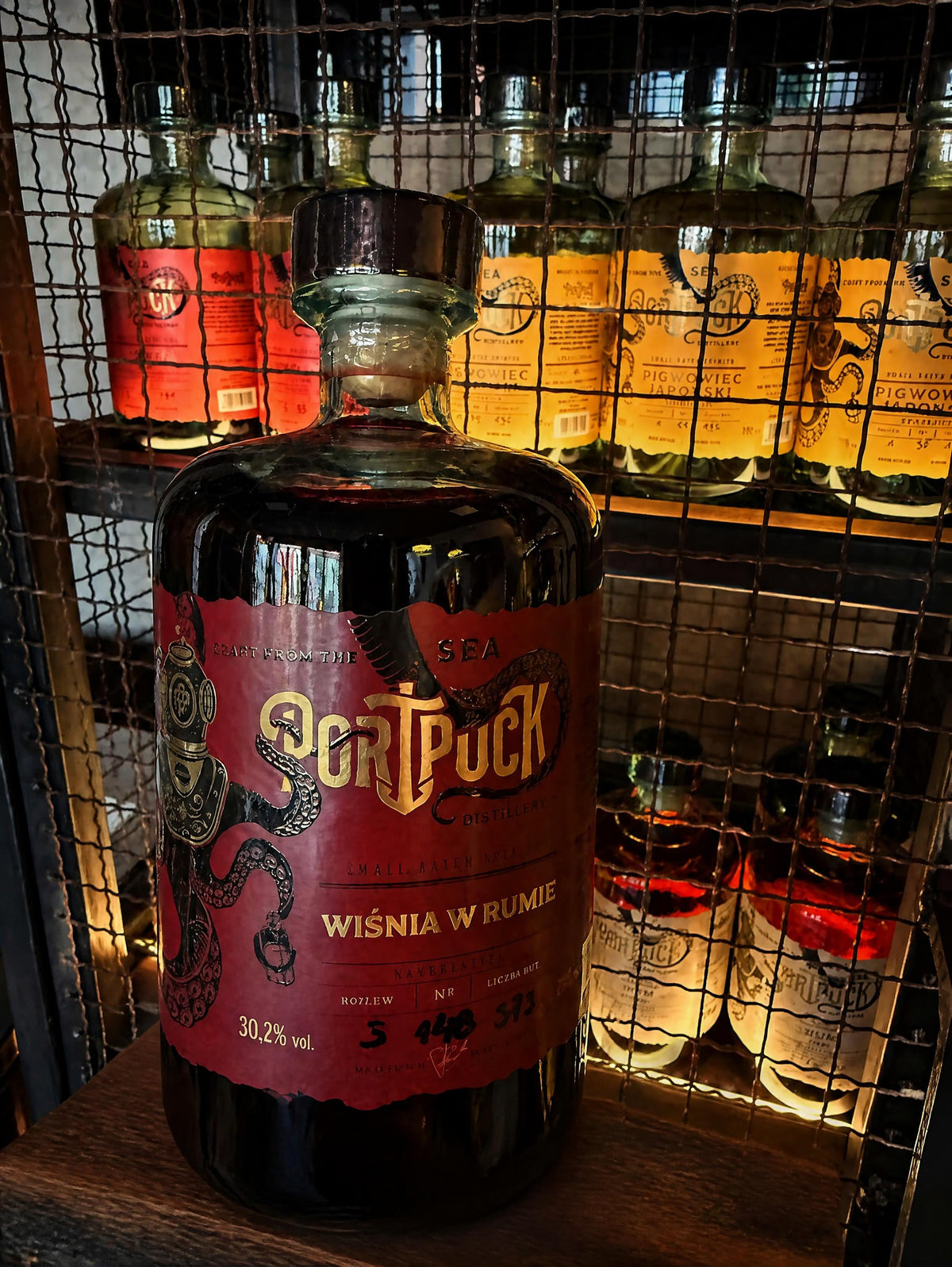 Butelka rzemieślniczej nalewki Wiśnia w Rumie z Port Puck Distillery, stojąca na drewnianej półce w klimatycznym barze.