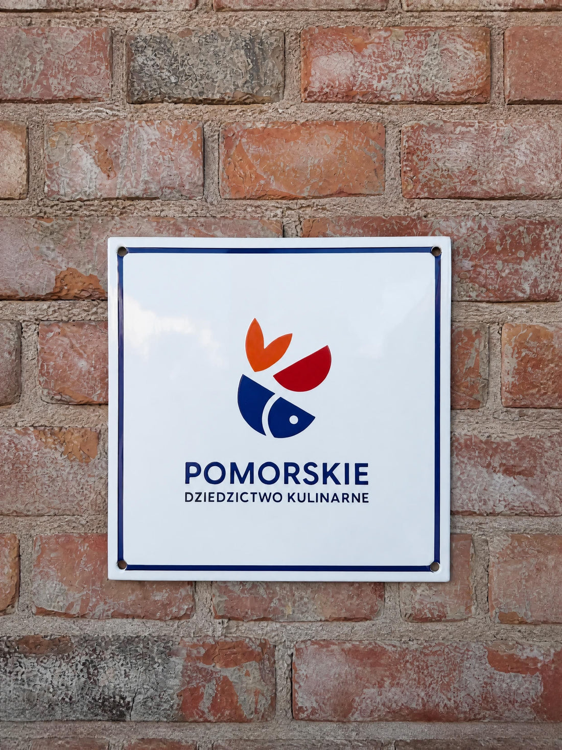 Tabliczka Certyfikatu Pomorskiego Dziedzictwa Kulinarnego na ceglanej ścianie Browaru Puck