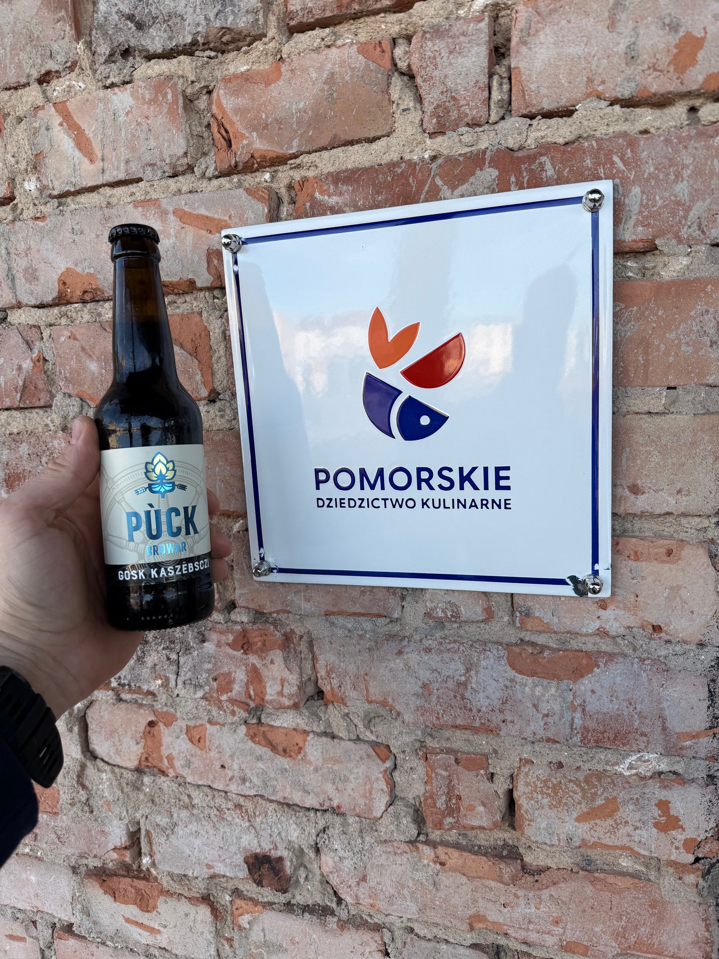 Butelka piwa Gòsk Kaszëbsczi Russian Imperial Stout 10,5% Browar Pùck obok tablicy Pomorskie Dziedzictwo Kulinarne